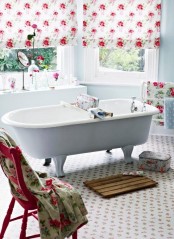 a cute vintage bathroom with a floral print floor, a white clawfoot bathtub, floral blinds, floral towels, a wooden mat and a floral box