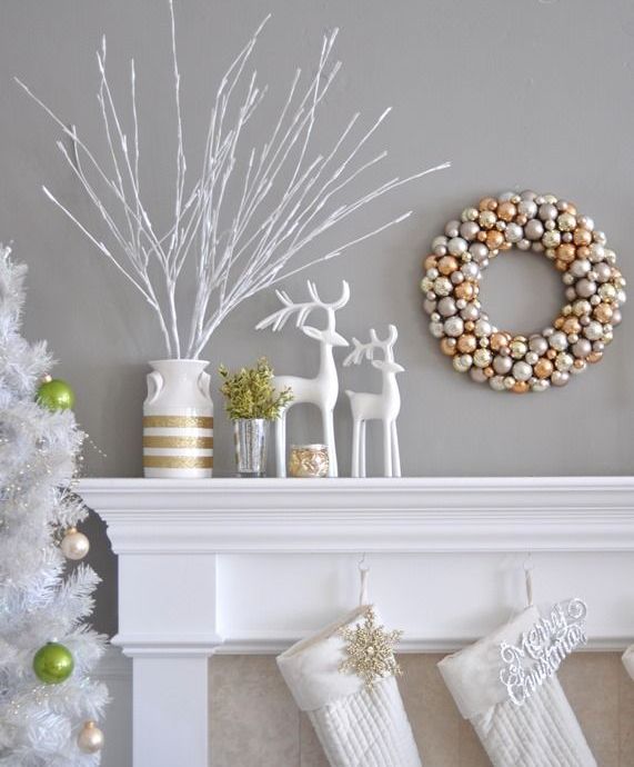 a silver and gold Christmas ornament wreath, white deer figurines, a white vase with gold stripes and a gilded candleholder