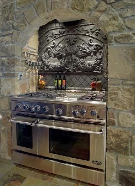 A light colored Gothic kitchen of light stone, a vintage backsplash and lights over the cooker