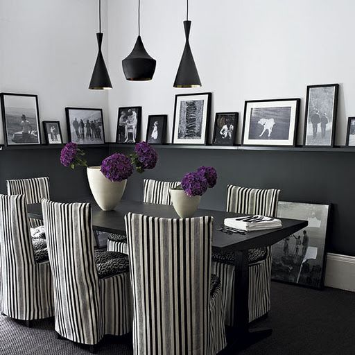 a modern Gothic dining room with black half walls, a black table, striped chairs, pendant black lamps and a gallery wall on the ledges