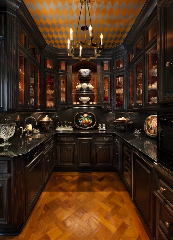 a moody Gothic kitchen in black, with vintage cabinets, a vintage chandelier, a bold geometric ceiling and vintage plates and bowls