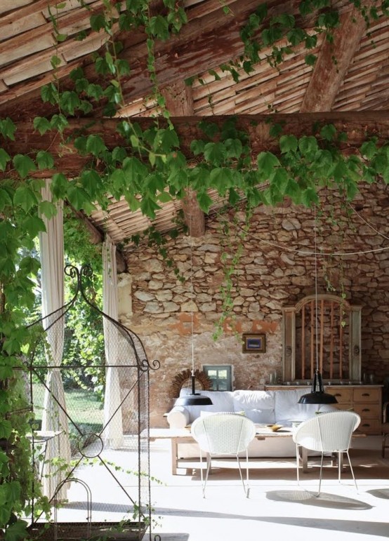 a Provence outdoor-indoor space with lots of vines, a white sofa, a coffee table and some chairs, a sideboard and vintage cages for decor