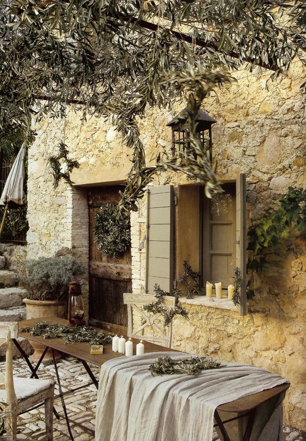A warm colored rustic Mediterranean terrace with a wooden table, a whitewashed chair, lots of potted greenery and trees around