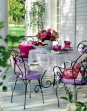 a Provence-inspired back porch with a whitewashed deck, a forged table and matching chairs, colorful cushions and pillows and a white tablecloth