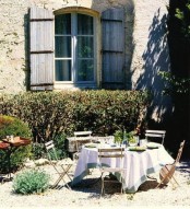 a simple sunlit Provence terrace with elegant bushes, a table and simple folding chairs, a side table to serve food and drinks