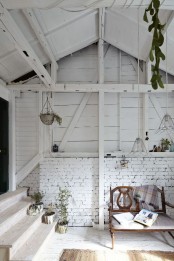an entryway with whitewashed wooden and brick walls, a slanted ceiling, pendant lamps and lots of potted plants is very refined