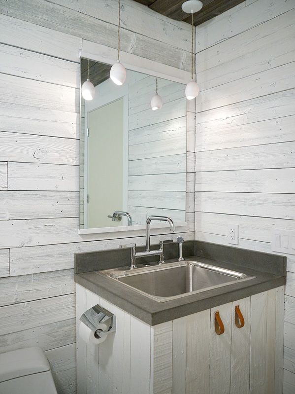 A farmhouse bathroom done with whitewashed wood, with pendant lamps, a whitewashed vanity and a metal sink plus a mirror with no frame