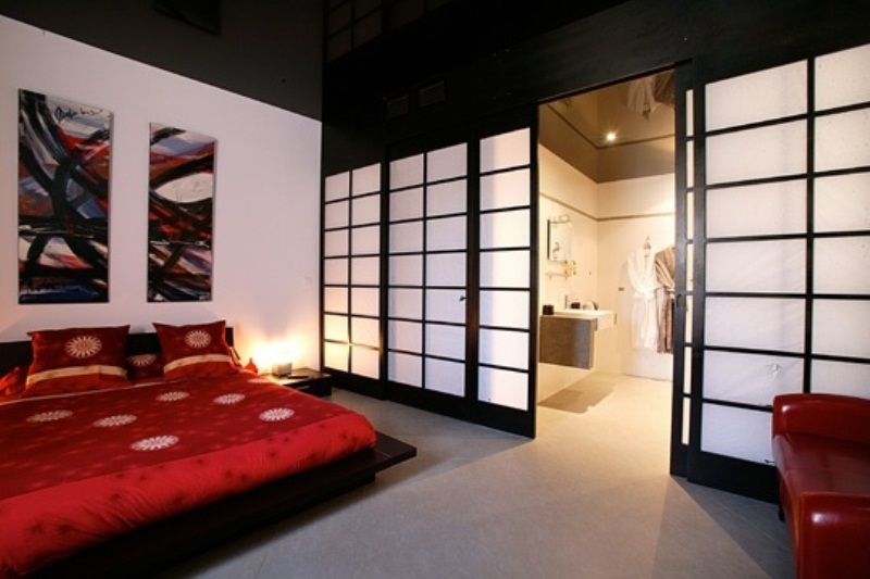 A bold Asian bedroom with a traditional zen feel, dark and red furniture, Asian sliding doors and bright bedding and a gallery wall in bright shades