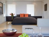 a modern zen bedroom with a dark bed and dark bedding, some statement artworks and a creamy sofa, a low table and drinks