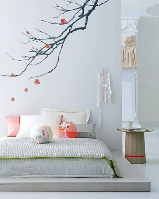 a romantic Japanese bedroom with a platform bed, pillows and blankets, a blooming branch on the wall and a pretty wooden nightstand