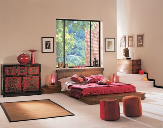 a colorful zen bedroom with a low wooden bed, a bright dresser, red ottomans, red lamps and candleholders and a large window