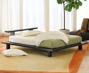 a neutral zen bedroom with a low black bed, a black leather chair, green and white bedding and a statement plant