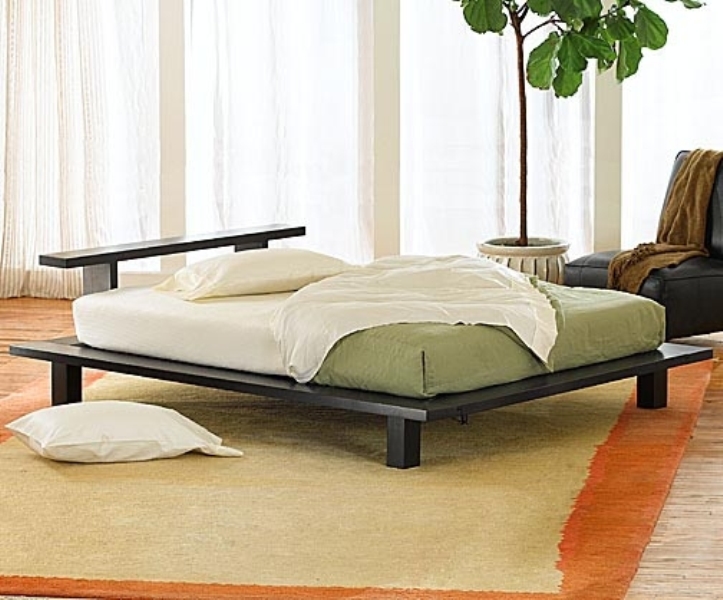 A neutral zen bedroom with a low black bed, a black leather chair, green and white bedding and a statement plant