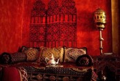 a hot red Moroccan living room with an orante screen on the wall, a bright sofa with pillows and a cool floor lamp
