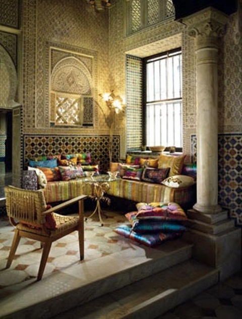 A gold Moroccan space with a super colorful L shaped sofa and bright pillows, mosaic walls and beautiful chairs