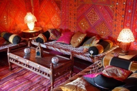 a super bright living room with fabric covered walls, bright textiles and a carved table in the center