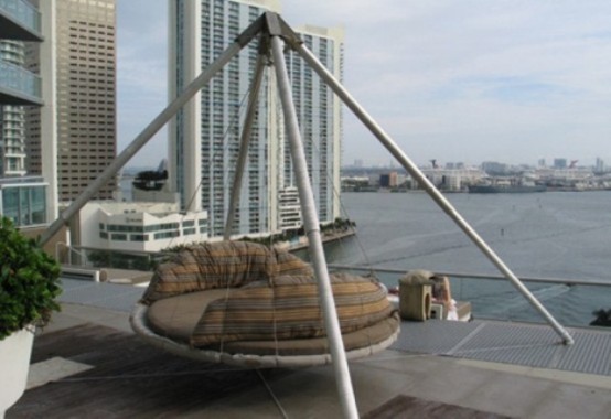 a metal hanging bed with a large base and ropes with striped pillows and cushions and a gorgeous view