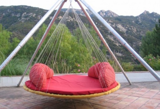 a round hanging bed with a proper base and red cushions and pillows is a cool idea for any outdoor space