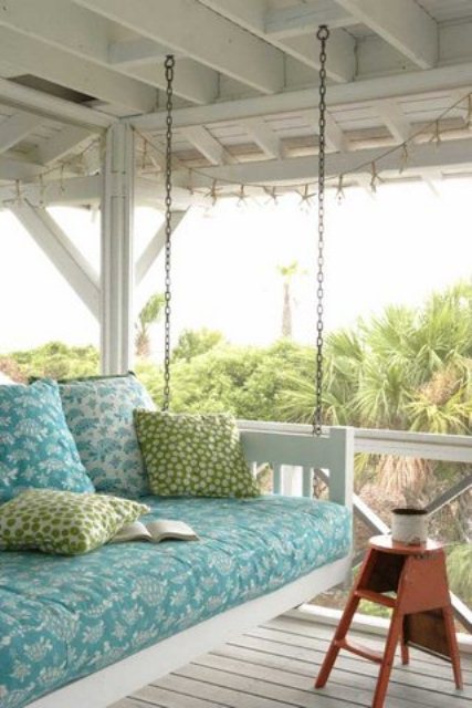 a comfortable white hanging bed with blue and green bedding is a cool idea for a rustic or vintage porch