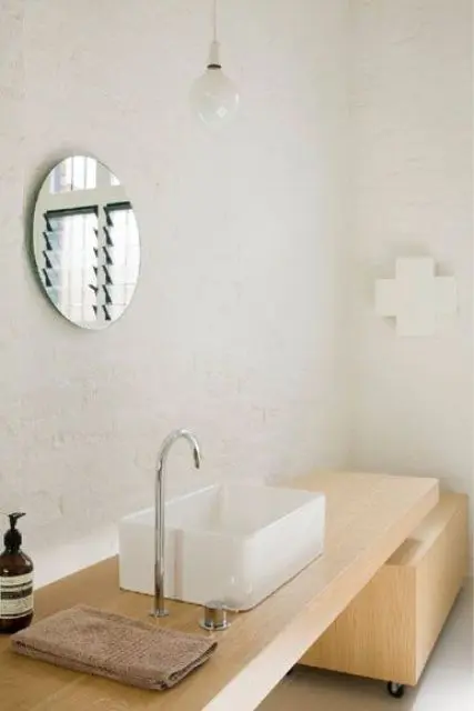 A neutral Scandinavian bathroom with white tiles, a light colored wooden vanity and a pendant bulb