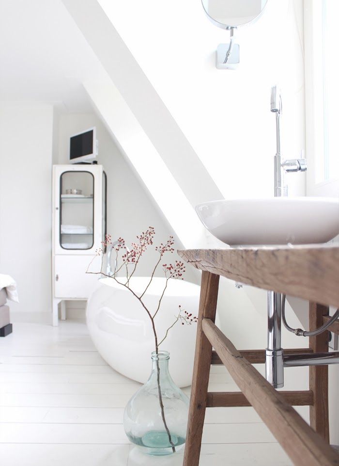 A beautiful Nordic bathroom with an oval tub and a bowl sink, a wooden vanity and an armoire for storage