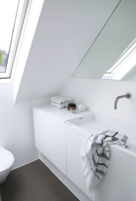 a small Nordic attic bathroom with a skylight, a built-in sink and a triangle mirror