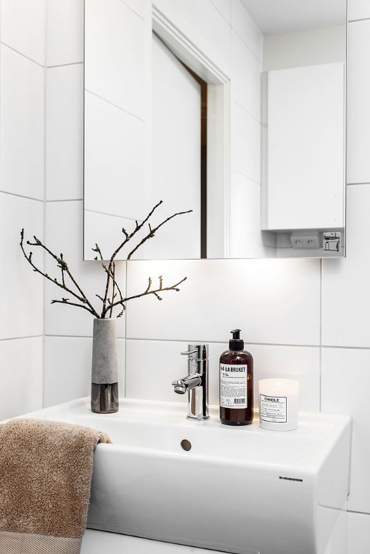 a Nordic bathroom with white tiles, a white sink, a large mirror and a branch arrangement