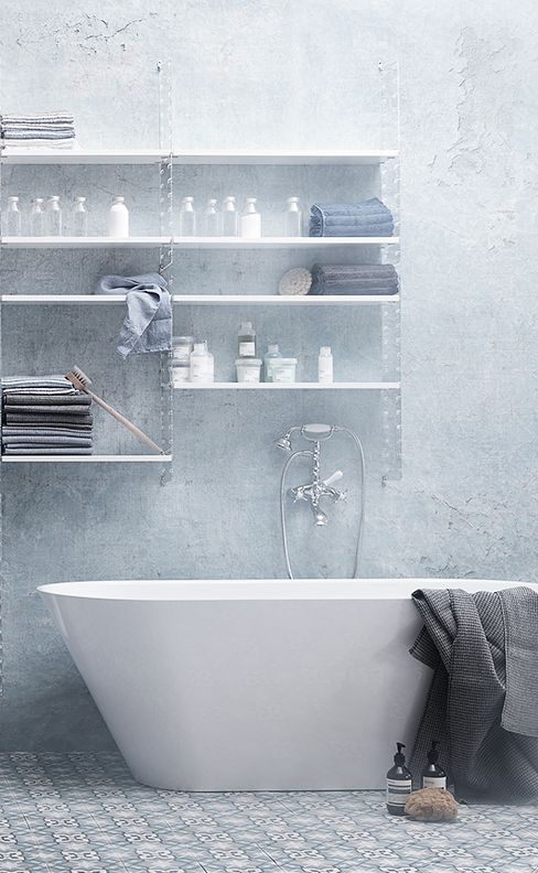 An off white and grey bathroom with mosaic tiles on the floor, a tub and a large open shelving unit