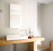 a light-colored wooden vanity, a rectangular mirror, a stool and a shower space with a wooden floor