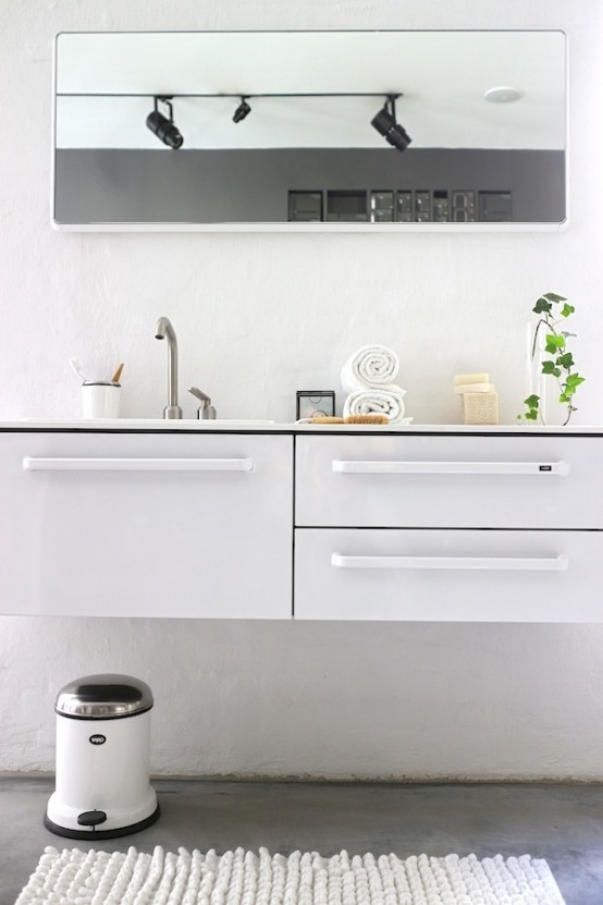 a casual Nordic bathroom with a white vanity, a large mirror, a white rug and a trash can