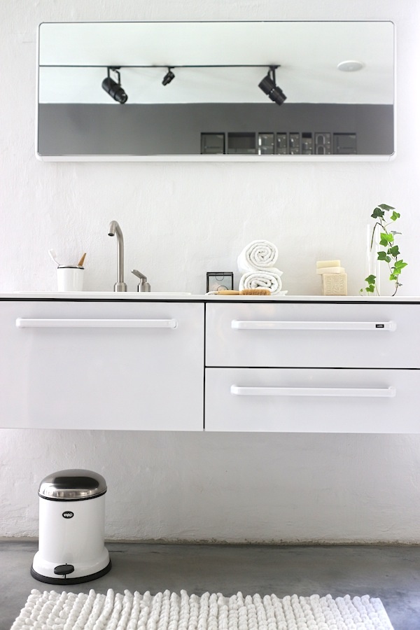 A casual Nordic bathroom with a white vanity, a large mirror, a white rug and a trash can