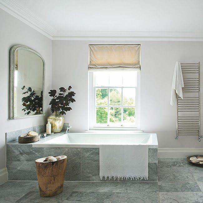 A grey and off white Scandinaviann bathroom with Roman shades, a large mirror and a tree stump table