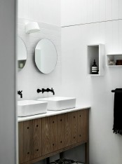 a simple Nordic bathroom done with white tiles, a wooden vanity and box shelves on the wall