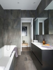 a minimalist bathroom with grey marble tiles all over, a graphite grey vanity and a large mirror