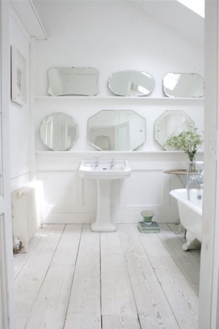 a clear and serene Nordic bathroom with a whitewashed wooden floor, lots of mirrors on display and a vintage tub