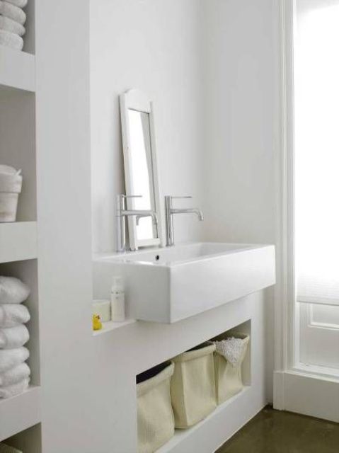 a minimalist white bathroom done with white concrete all over, a large sink and much storage space feels truly Nordic
