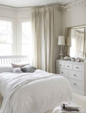 a neutral bedroom with soft-colored textiles, a mirror on a sideboard, neutral layered bedding is cool and chic