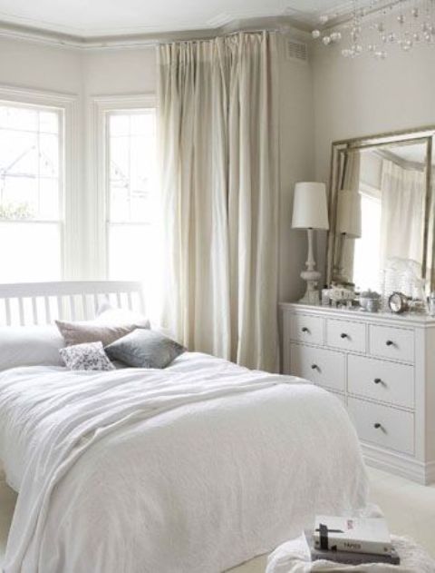 A neutral bedroom with soft colored textiles, a mirror on a sideboard, neutral layered bedding is cool and chic