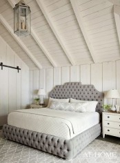 a neutral attic bedroom with a grey upholstered bed, white nightstands, pendant lamps and table ones