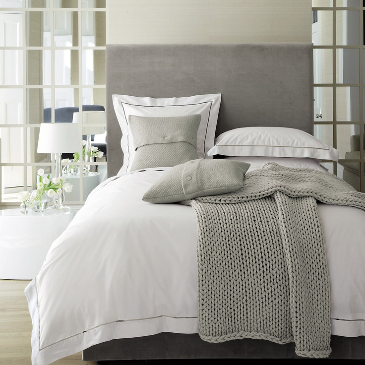 A modern bedroom with mirror panels, a grey bed, layered bedding and knit and crochet items is very light filled