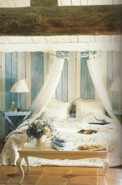 a Provence bedroom with blue and white planked walls, a bed with neutral bedding, a sheer canopy, blue vintage nightstands and a chic bench for storage at the foot of the bed
