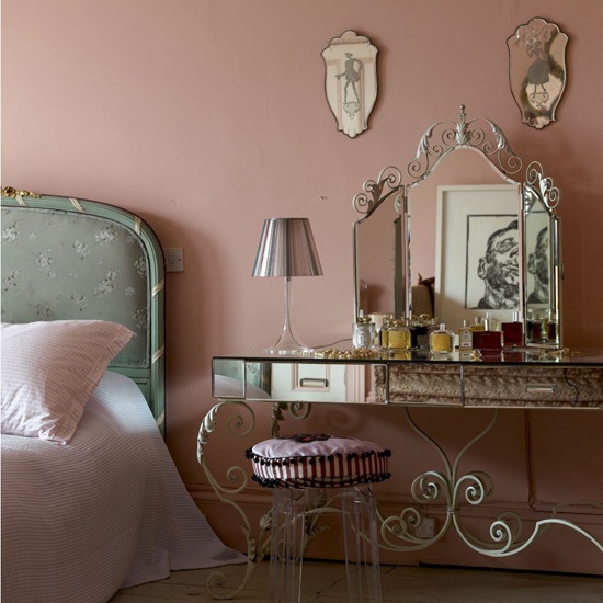 A pink French style boudoir bedroom with a blue floral bed, elegant vanity and a stool and some antique mirrors is lovely