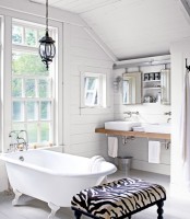 a white barn bathroom with wooden plank clad walls, a vintage lamp, a clawfoot tub, a printed ottoman and two mirrors