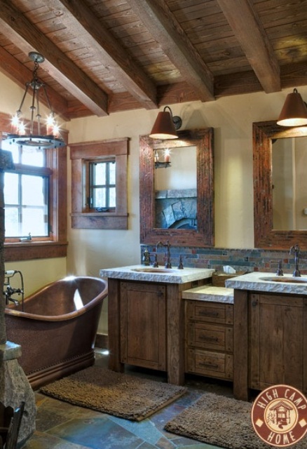 a barn bathroom with a wooden ceiling with beams, wooden furniture, a vintage metal tub and mirrors and windows in metal and wood frames