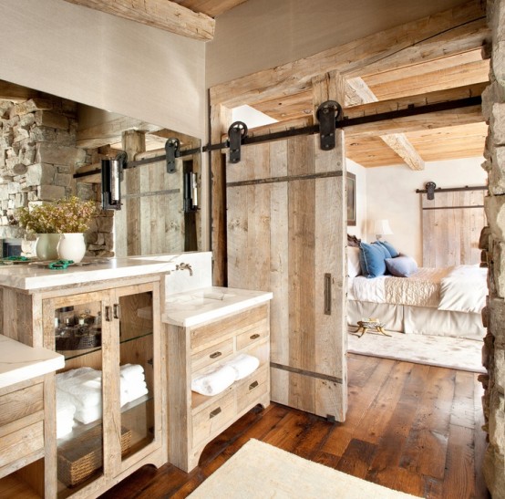 a barn bathroom with a sliding door, reclaimed wooden furniture, a large mirror and dried blooms in a vase