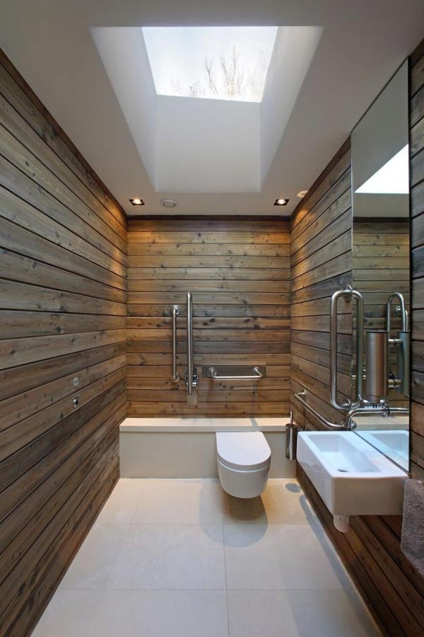 A minimalist barn bathroom clad with wooden planks, a large skylight, built in lights, a large mirror, a wall mounted sink