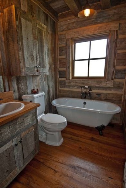 A barn bathroom fully clad with reclaimed wood, with a wall mounted cabinet, a clawfoot tub, a neutral sink and a window