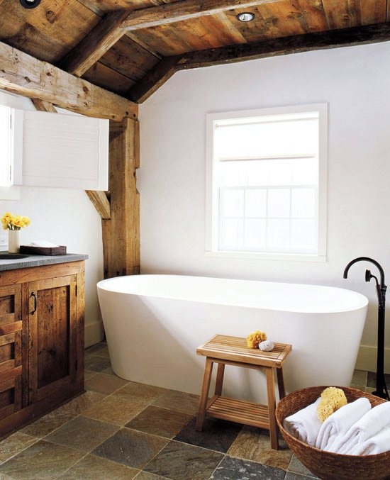 a rustic barn bathroom with a wooden ceiling, beams and furniture and a contemporary free-standing bathtub