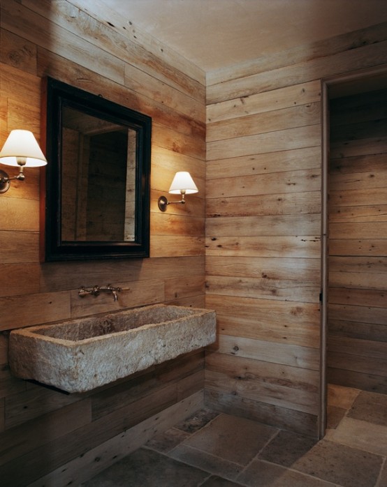 a very simple barn bathroom clad with wood, with a mirror and a stone wall-mounted sink
