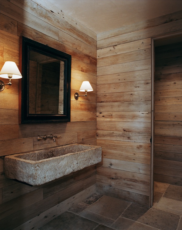 A very simple barn bathroom clad with wood, with a mirror and a stone wall mounted sink